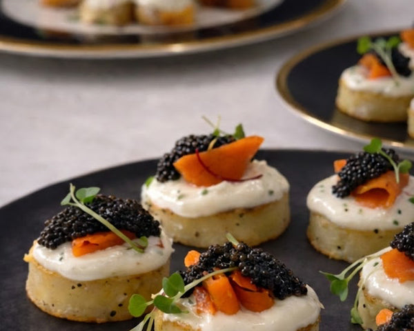 Delicate appetizers with caviar and salmon on a dark plate, set against a neutral background.